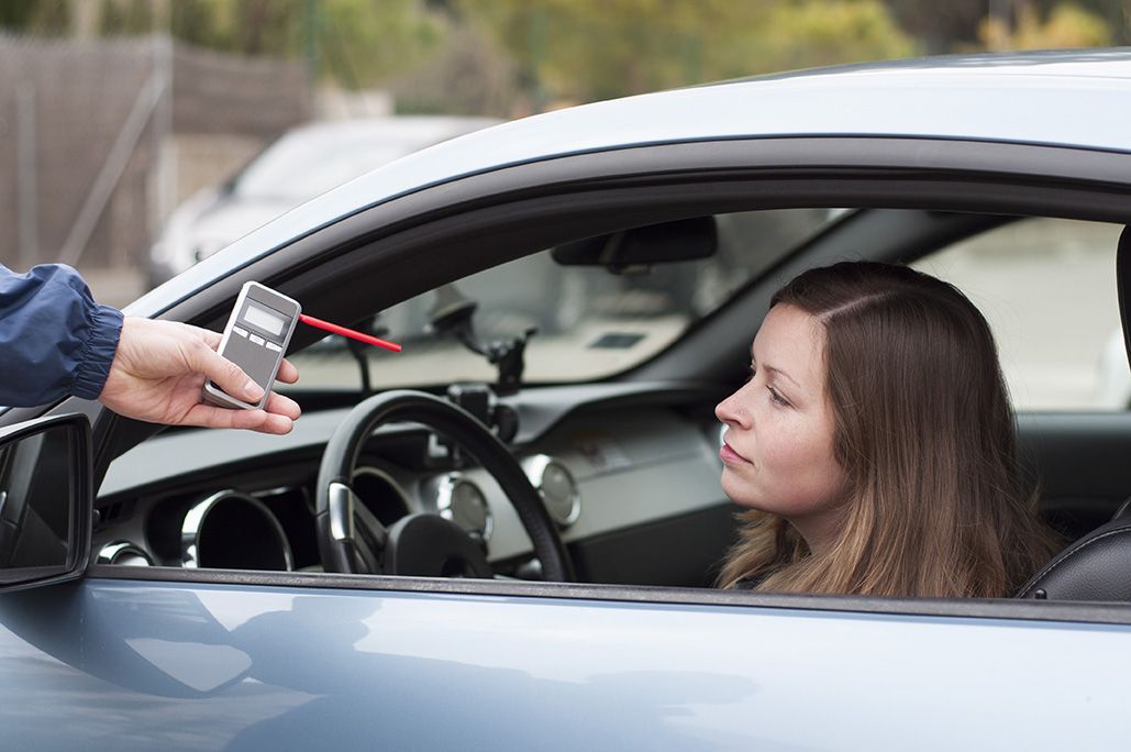 a police officer holding a breathalyzer for a woman in a car